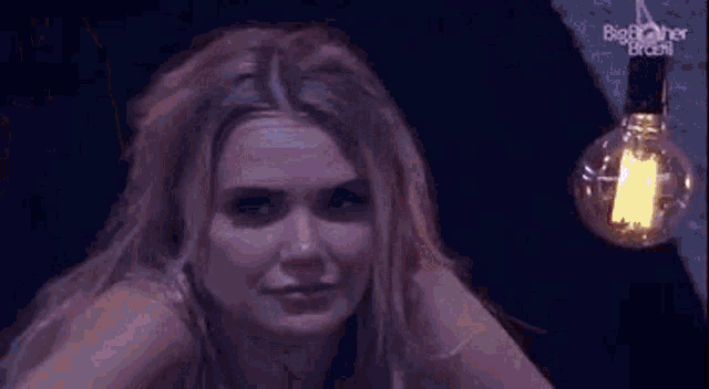 a close up of a woman 's face in a dark room with a light bulb hanging from the ceiling .