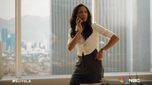 a woman talking on a cell phone in front of a window with #suitsla on the bottom right