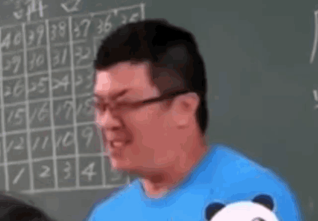 a man in a blue shirt is standing in front of a blackboard with numbers on it .