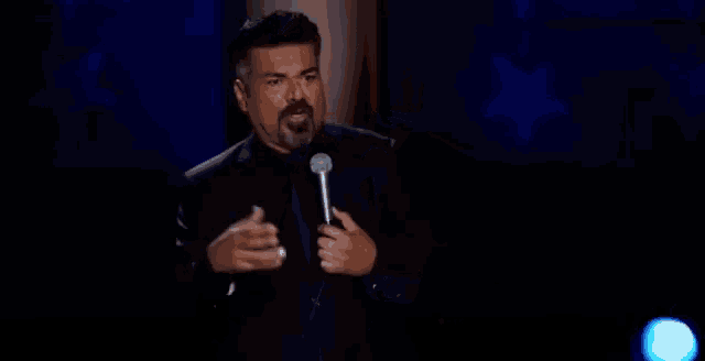 a man in a black suit is holding a microphone in his hand and talking into it .