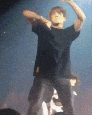 a man in a black shirt is dancing on a stage with his arms outstretched