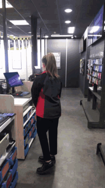 a woman in a red and black jacket stands in front of a counter in a store