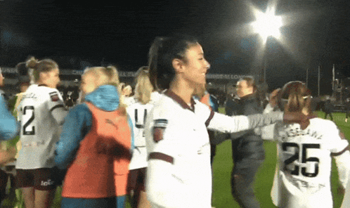 a woman wearing a number 25 jersey is hugging another woman on a soccer field