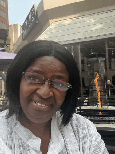 a woman wearing glasses is smiling in front of a sign that says ' grill ' on it