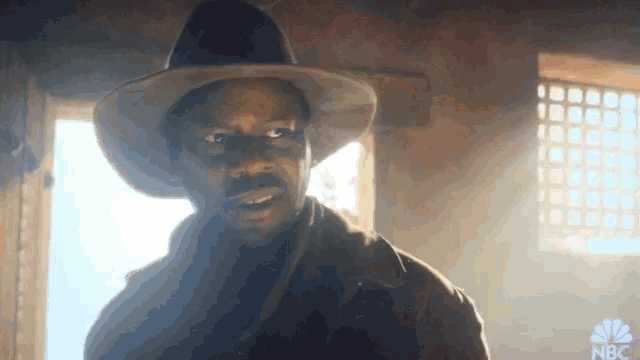 a man in a cowboy hat stands in front of a window with nbc written on it