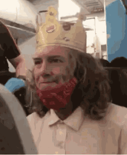 a man with long hair is wearing a burger king crown and a face mask .