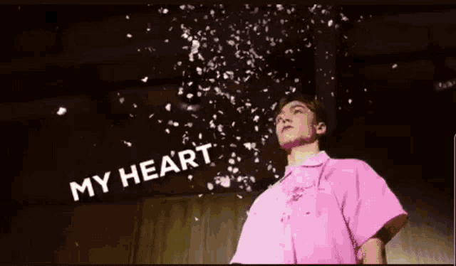 a man in a pink shirt is standing in front of a wall with confetti coming out of it .