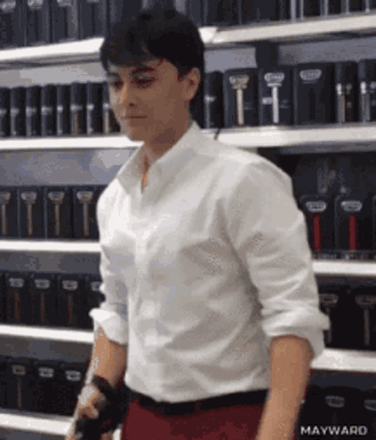 a man in a white shirt and red pants is standing in front of a shelf with bottles of shaving cream on it