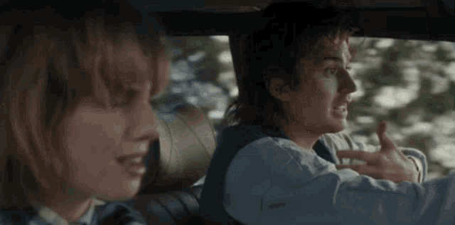 a man and a woman are sitting in a car and the man is giving a thumbs up .