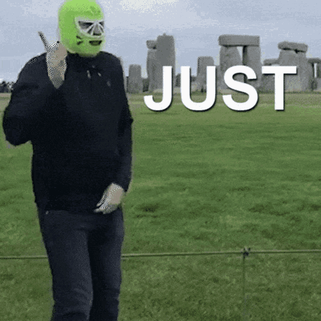 a man wearing a green mask is giving a thumbs up in front of a field that says just in white letters