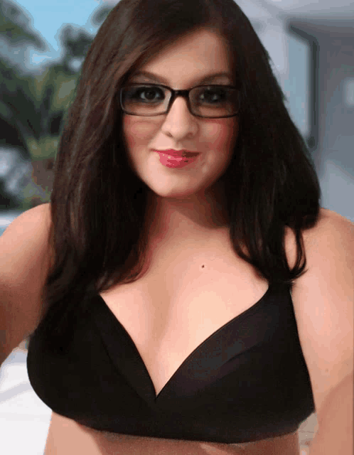 a woman wearing glasses and a black bra smiles for the camera