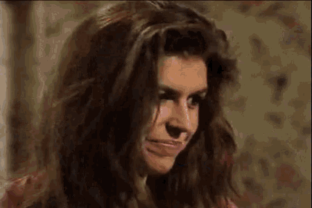 a woman with long hair is making a funny face while sitting in front of a wall .
