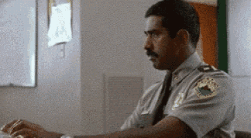 a man in a police uniform is sitting at a desk typing on a laptop computer .