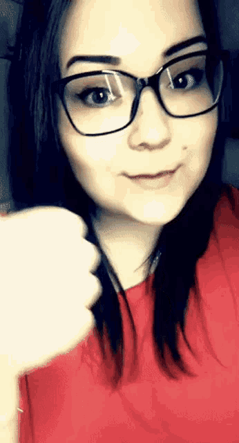 a woman wearing glasses is giving a thumbs down