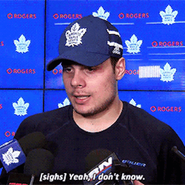 a man wearing a maple leaf hat talks into microphones