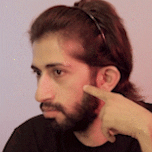 a man with a beard is pointing at his face with his finger