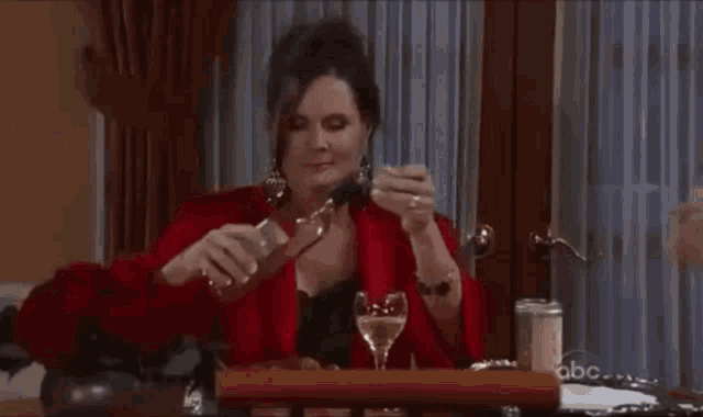 a woman in a red robe is sitting at a table holding a bottle of wine .