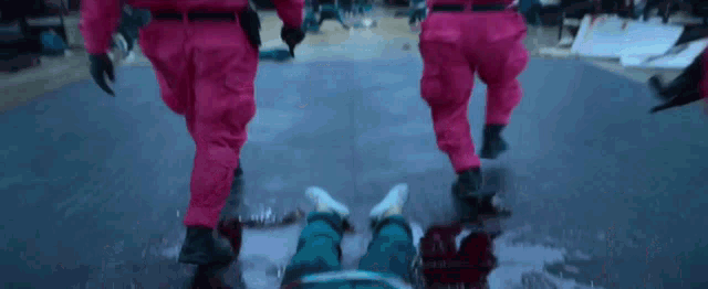 a group of people in pink jumpsuits are running towards a person laying on the ground covered in blood .