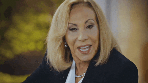 a woman with blonde hair is wearing a black jacket and pearl necklace