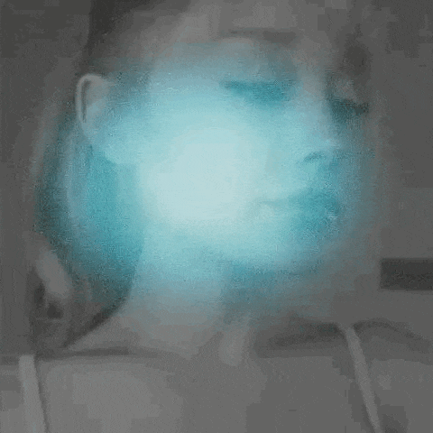 a woman 's face is glowing in the dark with a blue light coming out of it .