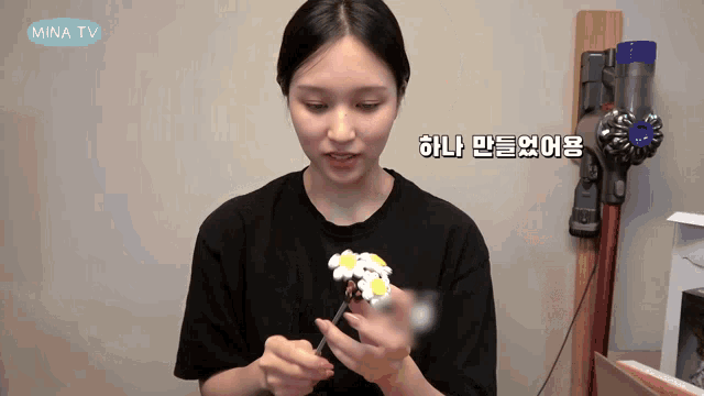 a woman is holding a flower in front of a vacuum cleaner that says mina tv on it