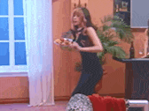 a woman in a black dress is dancing in a living room while holding a glass of wine .
