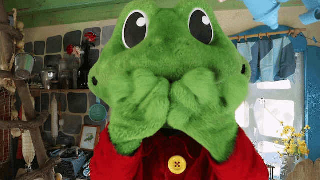a green stuffed animal with a yellow button on its collar