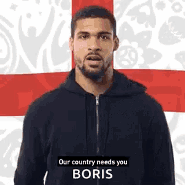 a man in a black hoodie is standing in front of a british flag and says `` our country needs you boris '' .