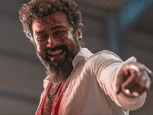 a man with a beard and blood on his face is pointing his finger at the camera .