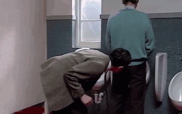 two men urinating in a public restroom with one of them looking down