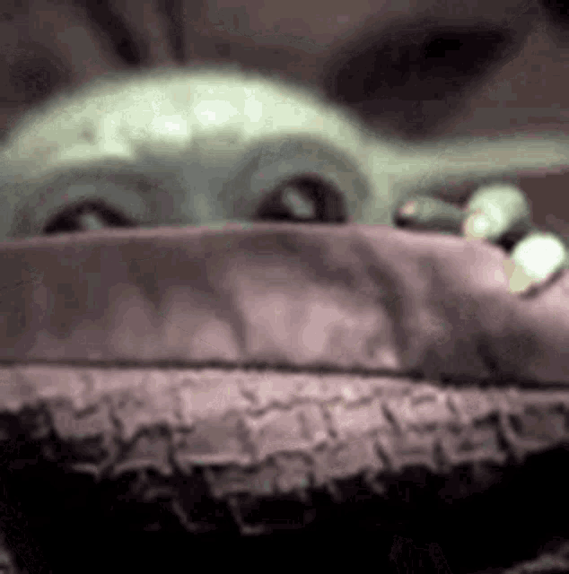 a close up of a baby yoda from star wars looking out from behind a blanket .