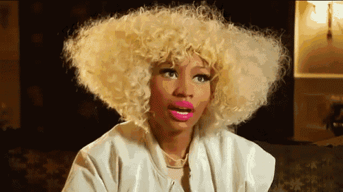a woman with blonde curly hair and pink lips is wearing a white jacket and necklace