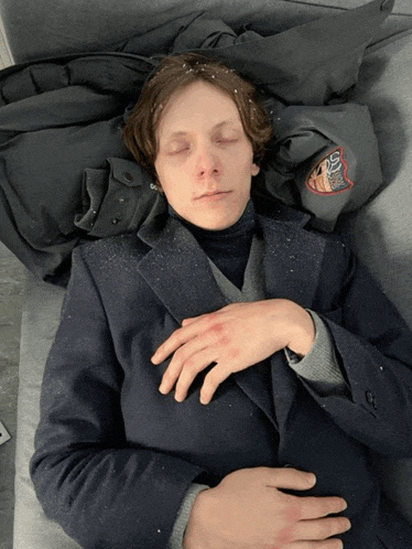 a man laying on a couch with his eyes closed and a jacket that says ' boston bruins ' on the back