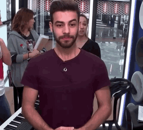 a man with a beard is standing in front of a piano and a microphone .