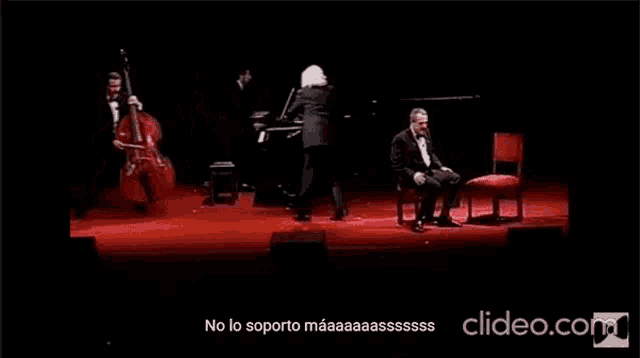 a man is sitting in a chair on a stage in front of a group of musicians