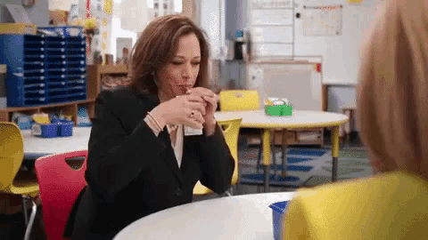 a woman sits at a table drinking from a cup