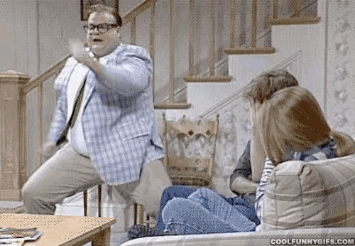 a man in a plaid jacket is dancing in front of a woman sitting on a couch .