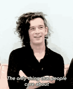 a man with curly hair is sitting on a couch with his arms crossed and says the only thing that people care about
