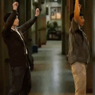 a man and a woman are dancing in a hallway with their arms in the air .