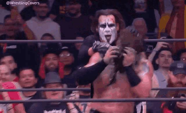 a wrestler with a mask on his face is standing in front of a crowd .