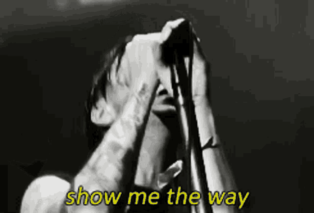 a black and white photo of a man singing into a microphone with the words show me the way below him