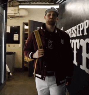 a man in a maroon jacket and white pants is walking down a hallway with mississippi written on the wall behind him