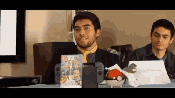 two men are sitting at a table playing a video game