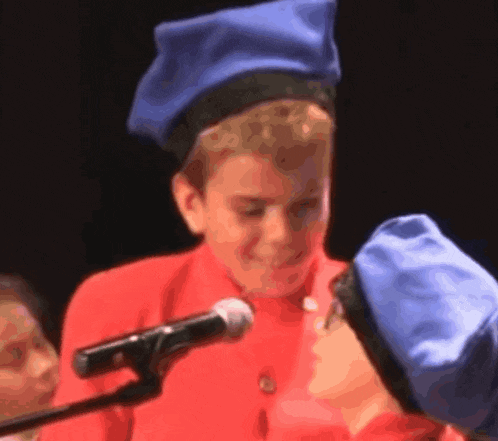a boy wearing a blue hat and a red shirt is speaking into a microphone