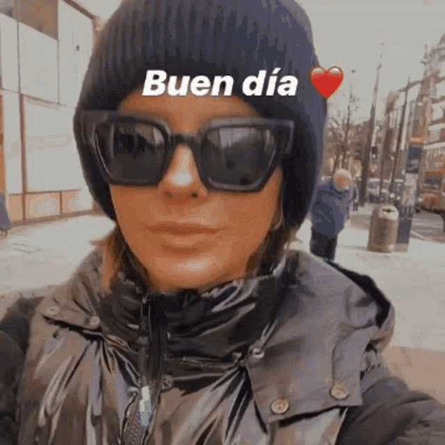 a woman wearing sunglasses and a beanie with the words buen dia written on it