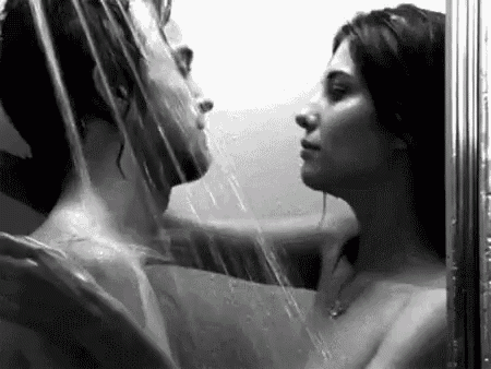 a black and white photo of a man and a woman kissing under a shower .