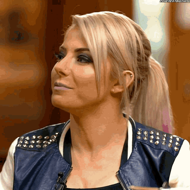 a close up of a woman 's face with a ponytail and a blue jacket with studs