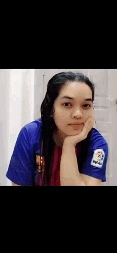 a woman wearing a blue shirt with the letter r on her arm is looking at the camera .
