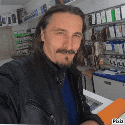 a man with long hair and a beard is wearing a black jacket and a blue shirt