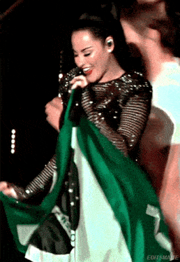 a woman singing into a microphone while holding a green and white flag behind her
